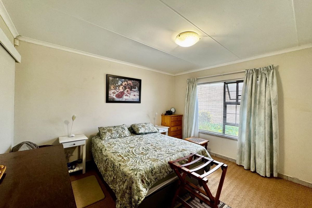 A functional bedroom featuring a window with blinds and curtains, neutral wall finishes, and carpeted flooring.