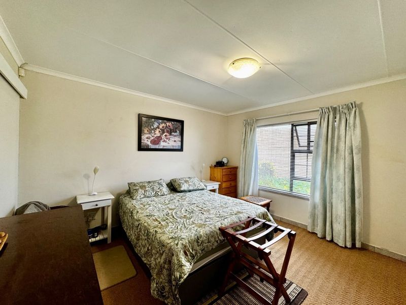 A functional bedroom featuring a window with blinds and curtains, neutral wall finishes, and carpeted flooring.