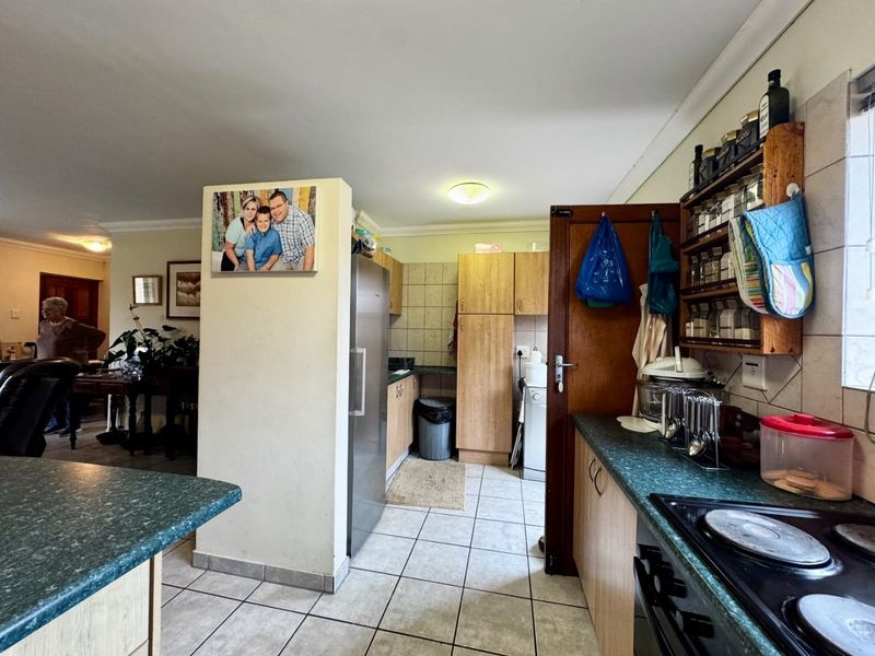 A functional kitchen featuring built-in cabinetry, laminate countertops, and an electric hob, with tiled flooring and backsplash throughout.