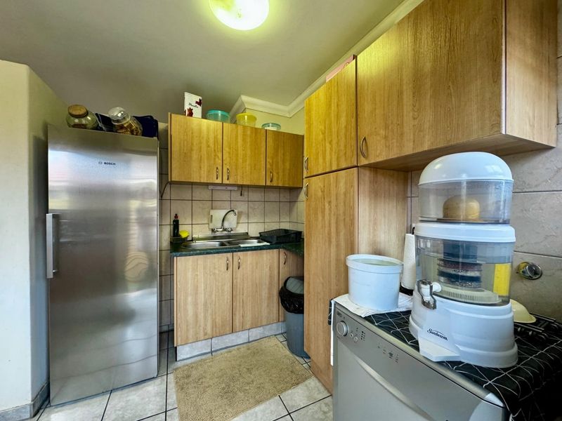 A functional scullery area featuring wood-look cabinetry, double sink, tiled backsplash, and tiled flooring, providing additional prep and storage space.