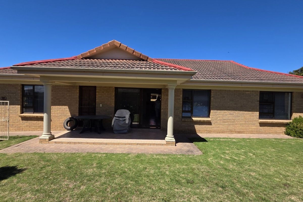 Rear view of a brick house featuring a covered patio with concrete columns, tiled roof, and a well-maintained lawn.
