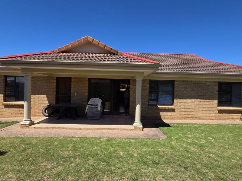 Rear view of a brick house featuring a covered patio with concrete columns, tiled roof, and a well-maintained lawn.