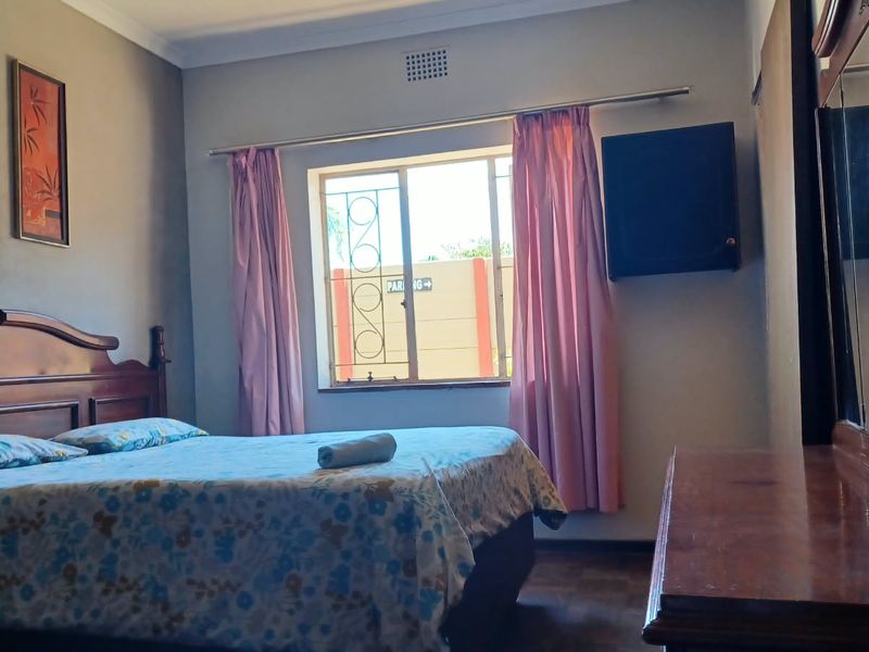 A standard bedroom featuring a window with security burglar bars, neutral wall finishes, and a built-in ventilation grille.