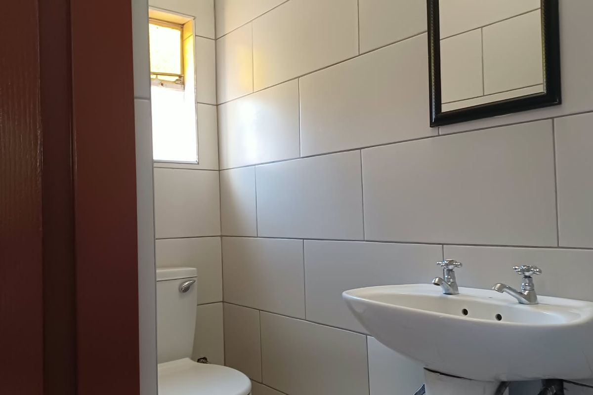 A functional bathroom featuring white wall tiles, a wall-mounted basin with dual-handle faucets, and a standard toilet.