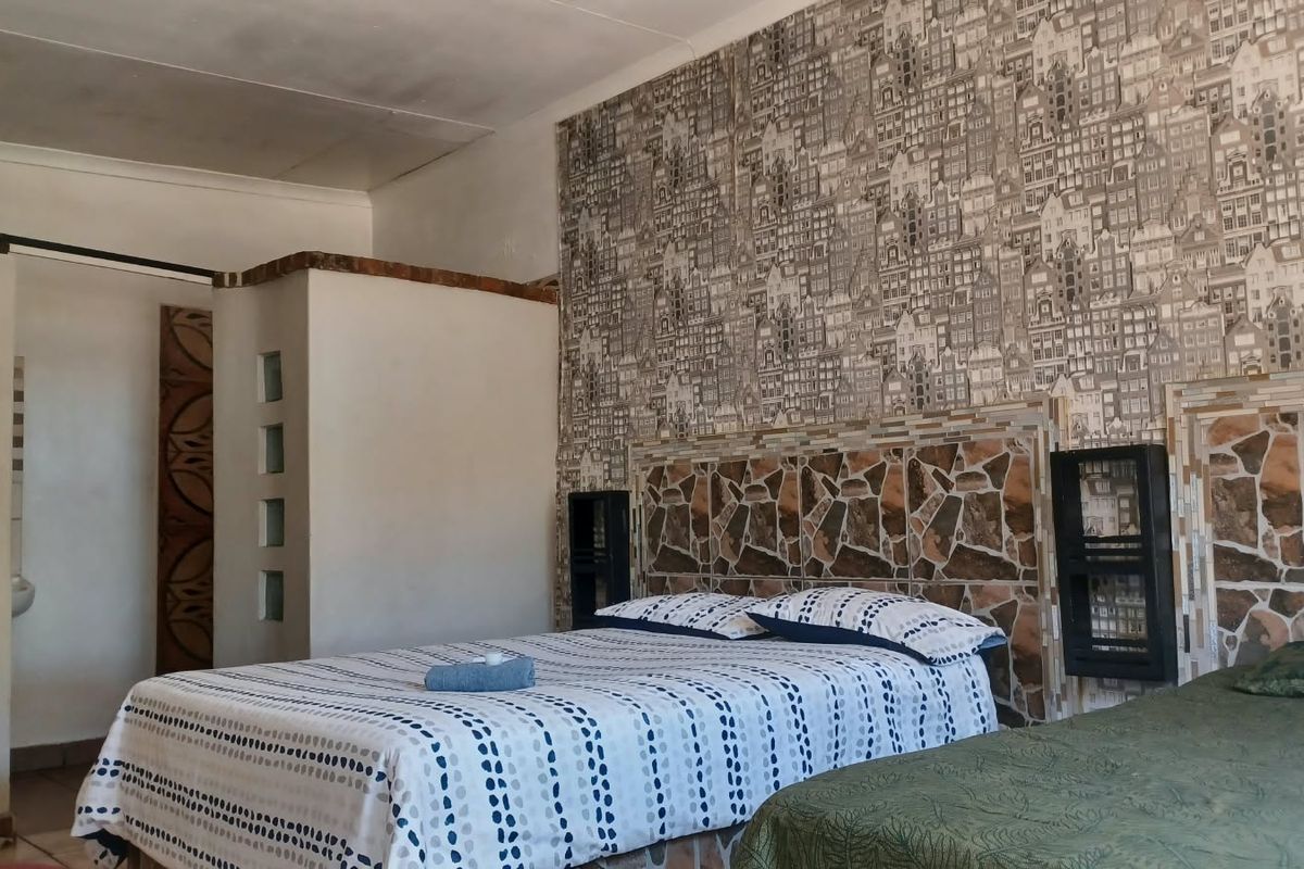 Bedroom featuring a unique stone-tiled headboard, decorative wallpaper, and a partition wall with glass block accents.