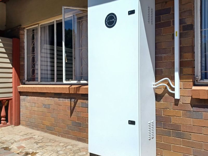 Exterior view of a brick building featuring a wall-mounted solar battery storage unit and security-fitted windows.