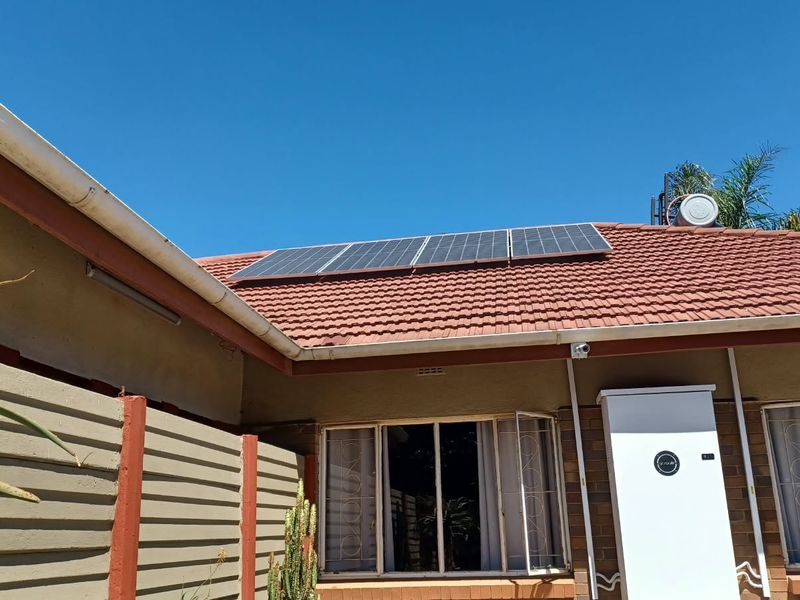 Rear exterior view of the property featuring a tiled roof with installed solar panels, security camera, and an external battery storage unit.