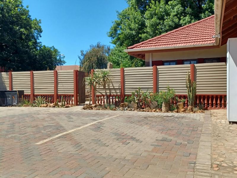 A paved rear courtyard area featuring a secure perimeter wall, brick building facade, and a tiled roof structure.