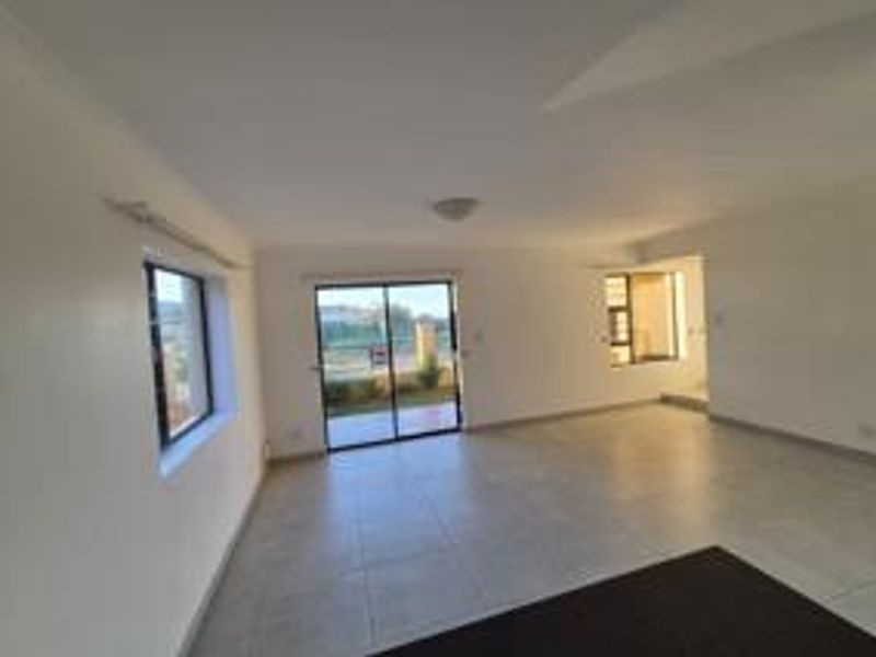A spacious, empty living area featuring neutral tiled flooring, a sliding glass door leading to the exterior, and clean white walls.