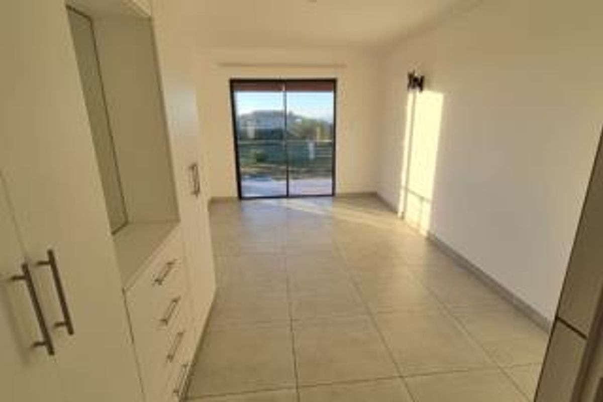 A bright, empty bedroom featuring neutral tiled flooring, built-in cupboards, and a sliding glass door providing natural light and outdoor access.