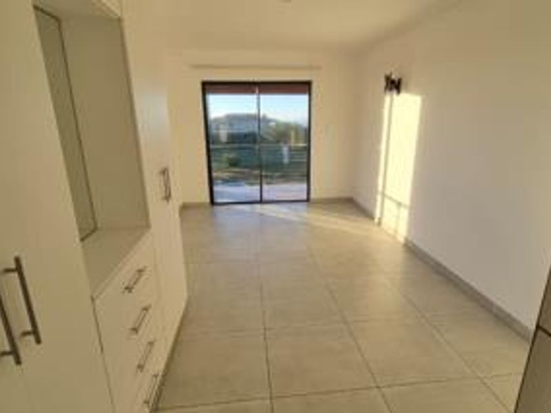 A bright, empty bedroom featuring neutral tiled flooring, built-in cupboards, and a sliding glass door providing natural light and outdoor access.