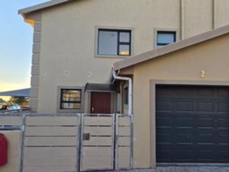 Front elevation of a townhouse featuring a single garage, pedestrian gate, and boundary wall with visible exterior finishes.