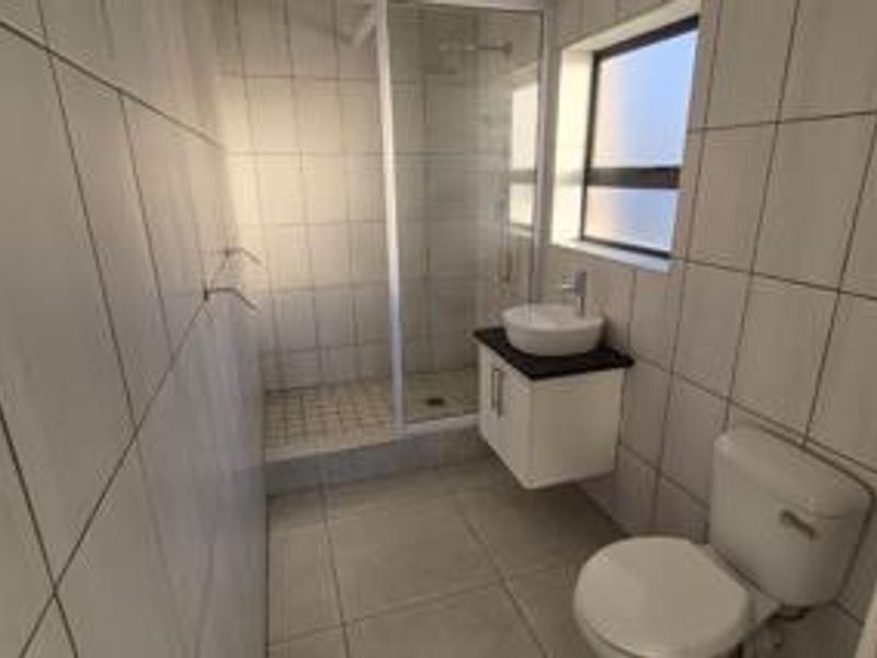 A clean, modern bathroom featuring a glass-enclosed shower, wall-mounted vanity with a vessel sink, and neutral floor-to-ceiling tiling.
