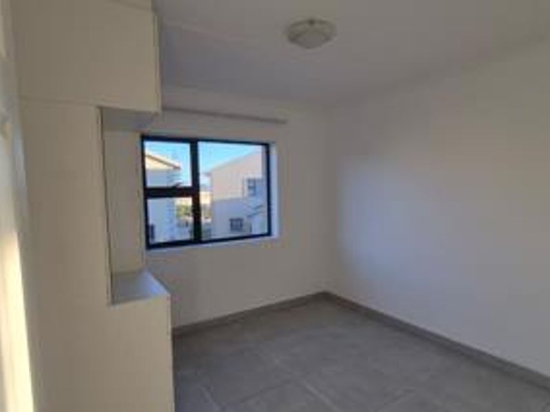 A bright, empty bedroom featuring neutral tiled flooring, built-in cupboards, and a modern aluminium-framed window.