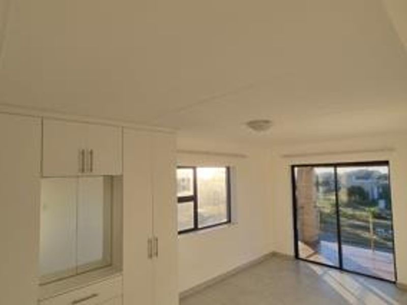 A bright, empty bedroom featuring built-in cupboards, tiled flooring, and a sliding glass door leading to an outdoor area.