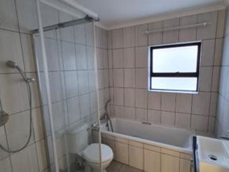 A functional bathroom featuring a shower enclosure, bathtub, toilet, and wall-mounted basin with tiled finishes throughout.