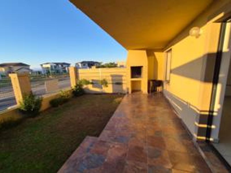 A covered patio area featuring a built-in braai, tiled flooring, and direct access to a small garden space.