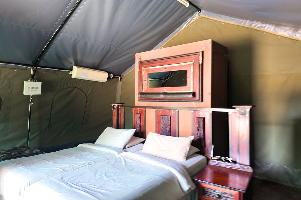 A bedroom interior within a canvas tent structure, featuring a wall-mounted split-system air conditioner and integrated electrical distribution board.
