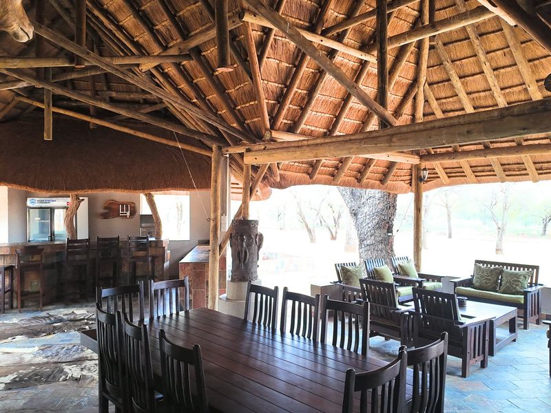 Spacious outdoor entertainment area featuring a traditional thatched roof, exposed timber trusses, built-in bar, and tiled flooring overlooking the farm landscape.