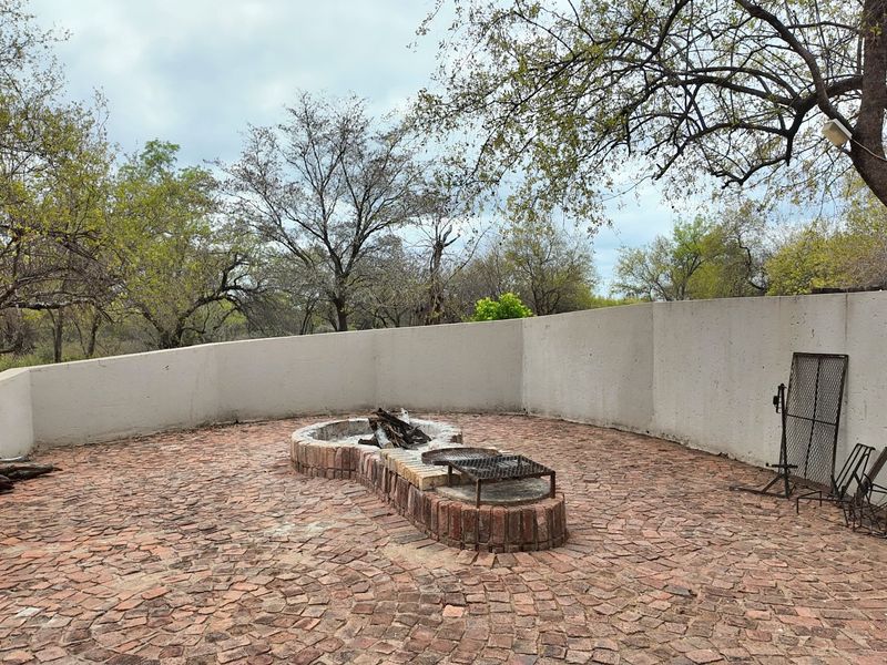 Outdoor entertainment area featuring a brick-paved patio, a built-in fire pit, and a built-in braai, enclosed by a curved retaining wall.