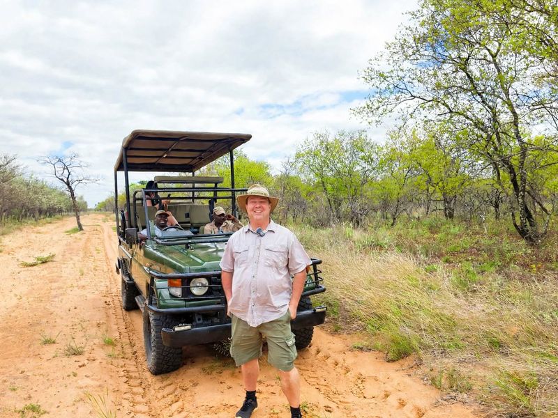 A view of a safari vehicle on a dirt track within a natural bushveld landscape.