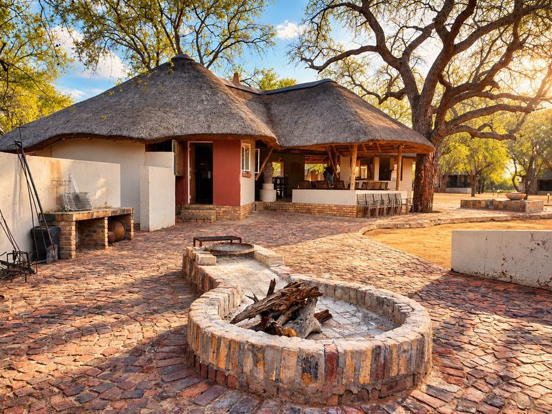 A spacious outdoor entertainment area featuring a thatched roof dwelling, brick paved patio, built-in fire pit, and a built-in braai station.