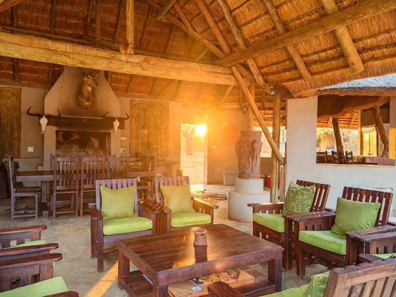 Spacious covered outdoor patio featuring a traditional thatched roof, exposed timber beams, and a large built-in fireplace, perfect for relaxed farm-style entertaining.