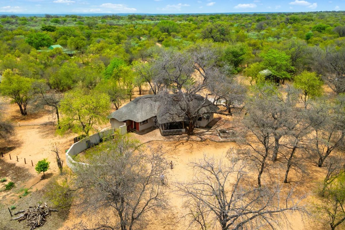 Aerial view of a farm property featuring a main dwelling with a traditional thatch roof, surrounded by natural bushveld and a perimeter wall.