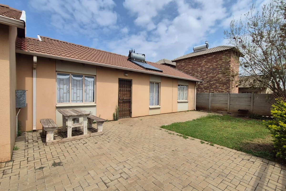 Rear exterior view of the house featuring a paved patio area, solar water heater, and a small garden with perimeter walling.