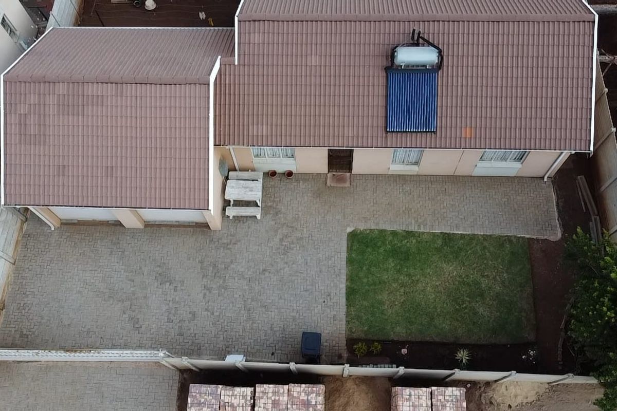 Aerial view of the property featuring a tiled roof with a solar water heater, paved driveway, small lawn, and perimeter boundary wall.