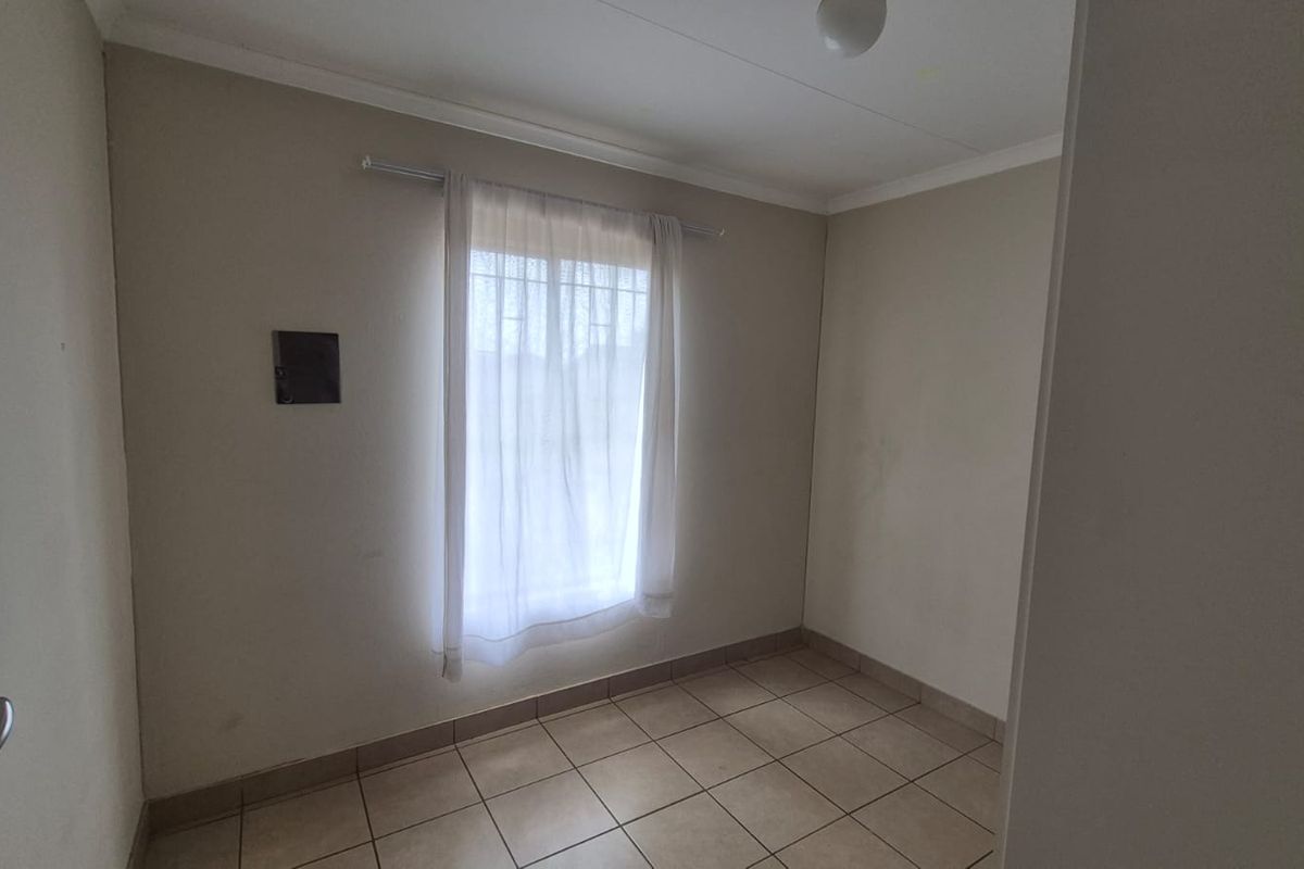 A vacant bedroom featuring neutral tiled flooring, a window with security bars, and a curtain rod, offering a blank canvas for personalization.