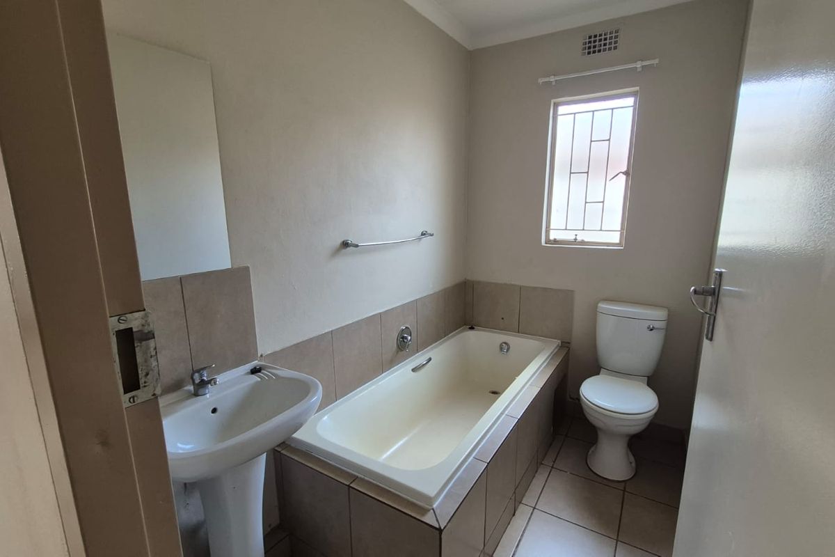 A functional bathroom featuring a pedestal basin, built-in bathtub, and toilet with tiled flooring and splashbacks.