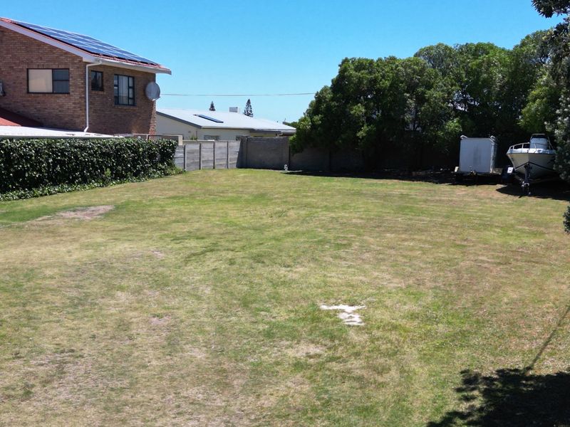 A spacious, level residential plot featuring a grass lawn, mature trees, and established precast concrete boundary walls.