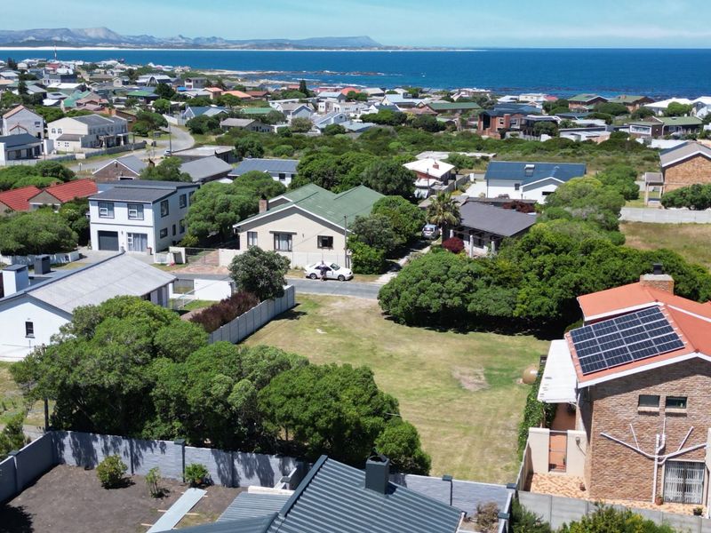 Aerial view of a vacant residential plot situated in a coastal neighborhood, featuring established greenery and proximity to the ocean.