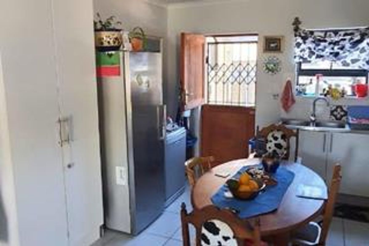 A functional kitchen area featuring built-in cabinetry, a stainless steel sink, and tiled flooring, with direct access to an exterior door with a security gate.