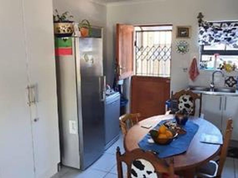 A functional kitchen area featuring built-in cabinetry, a stainless steel sink, and tiled flooring, with direct access to an exterior door with a security gate.