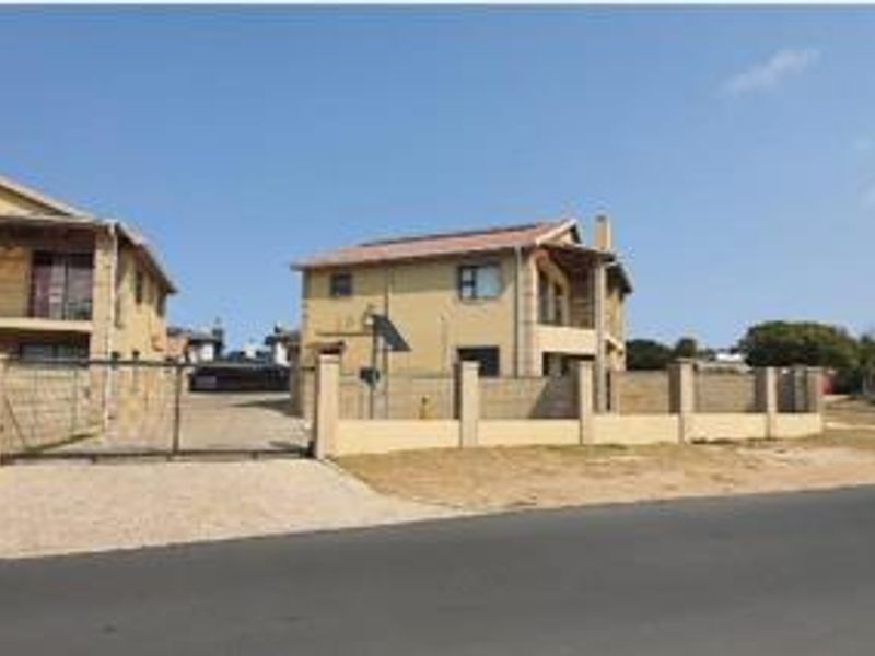 Front exterior view of a townhouse complex featuring a paved driveway, perimeter walling, and gated access.