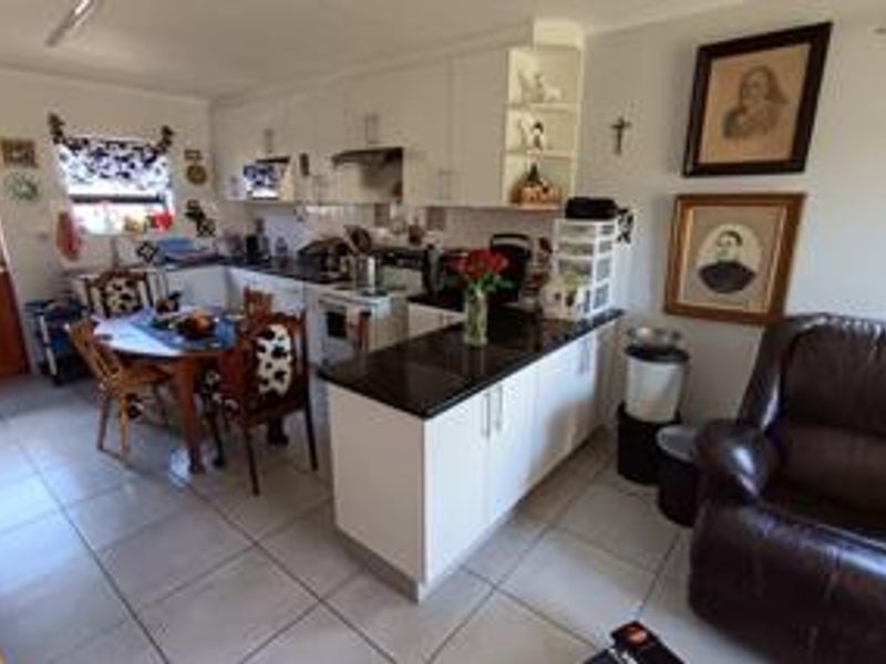 Open-plan kitchen and living area featuring white cabinetry, granite countertops, and neutral ceramic floor tiles throughout the space.