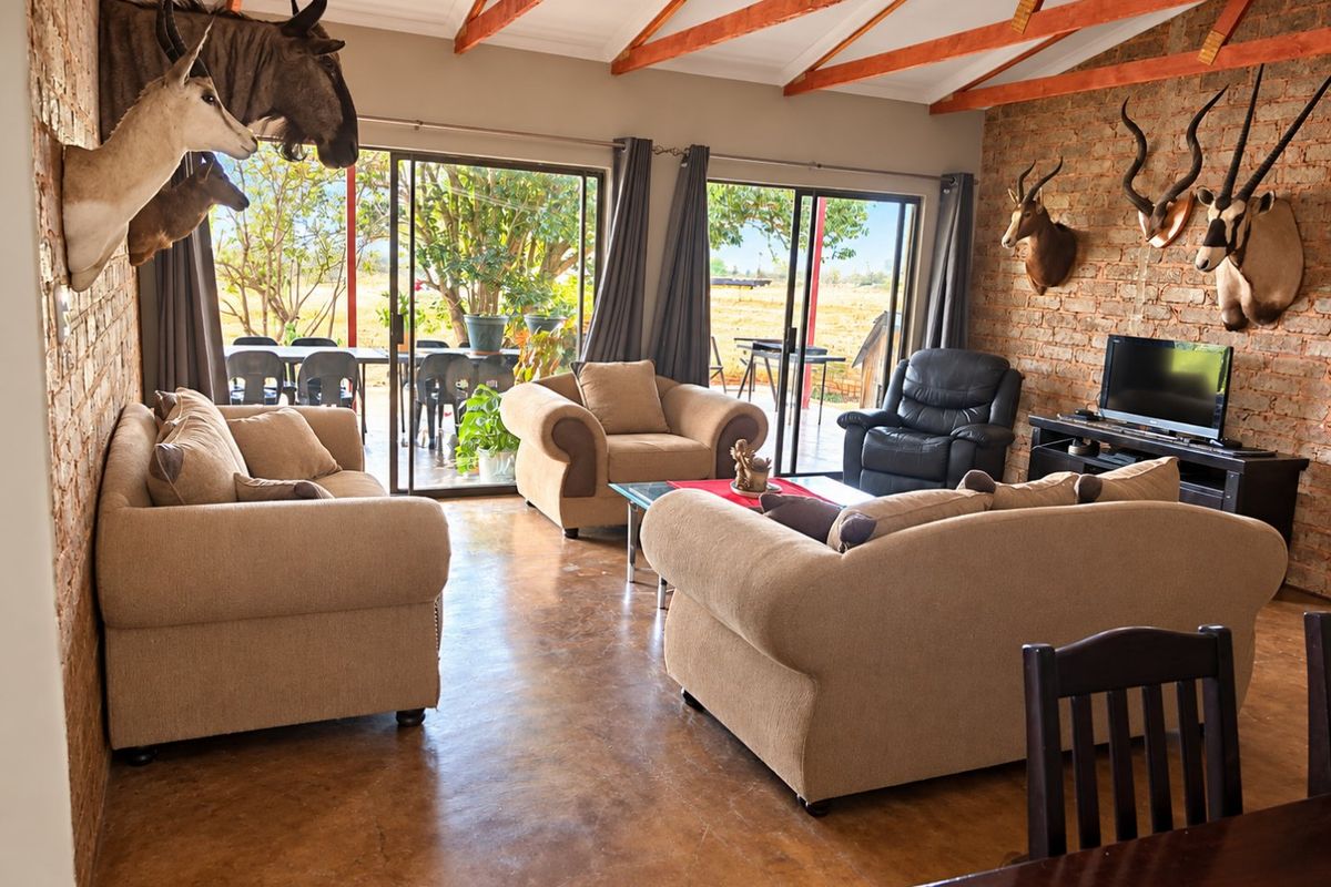 Spacious living room featuring polished concrete floors, exposed brick walls, and high ceilings with timber trusses, opening onto a covered patio area.