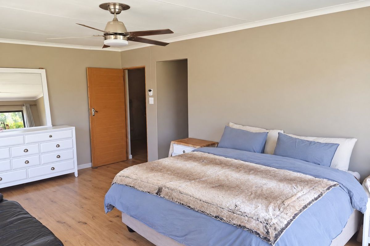 A spacious bedroom featuring neutral wall tones, laminate flooring, and a ceiling fan, offering a comfortable and well-maintained living space.