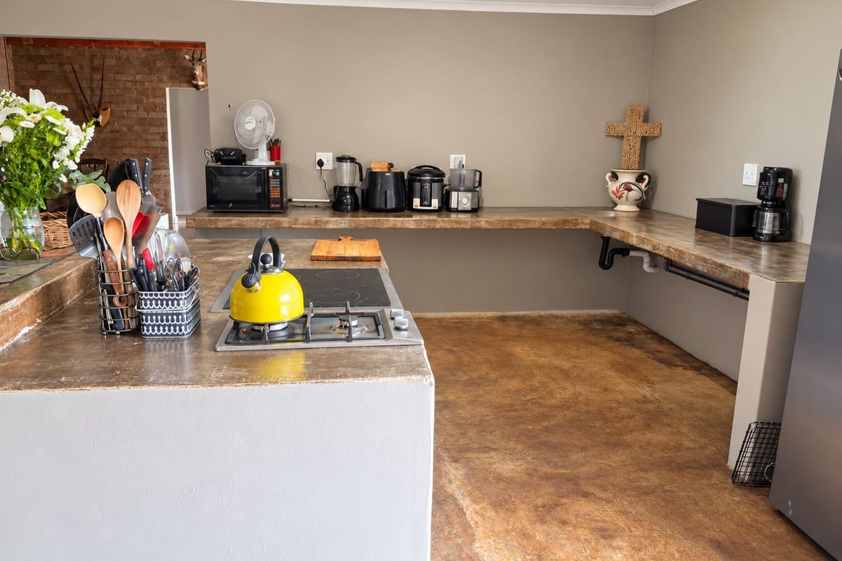 A rustic kitchen featuring built-in concrete countertops, a dual gas and electric hob, and polished concrete flooring with an adjacent exposed brick wall.