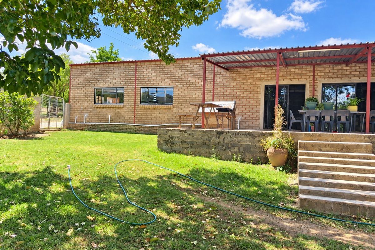 Rear view of a face brick farmhouse featuring a covered patio area, concrete steps, and a spacious garden setting.