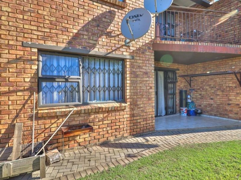 Rear exterior view of the apartment featuring a face brick facade, a paved patio area, and an upper-level balcony with metal railings.