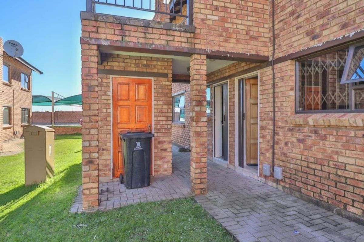Rear exterior view of the apartment featuring a paved patio area, face brick facade, and secure access points with security bars.