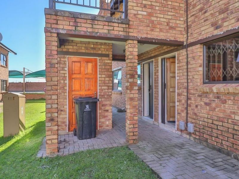 Rear exterior view of the apartment featuring a paved patio area, face brick facade, and secure access points with security bars.