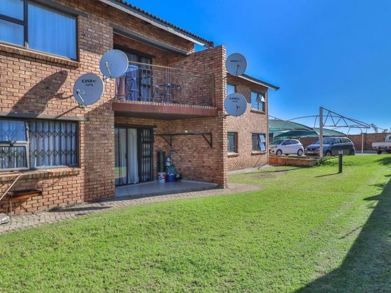 Rear view of a face brick apartment building featuring a ground floor patio, upper level balcony with metal railing, and a shared lawn area.