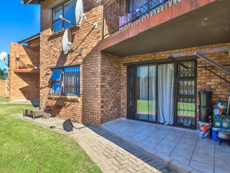 Rear view of the apartment building featuring a face brick facade, a tiled patio area, and sliding glass doors with security bars.