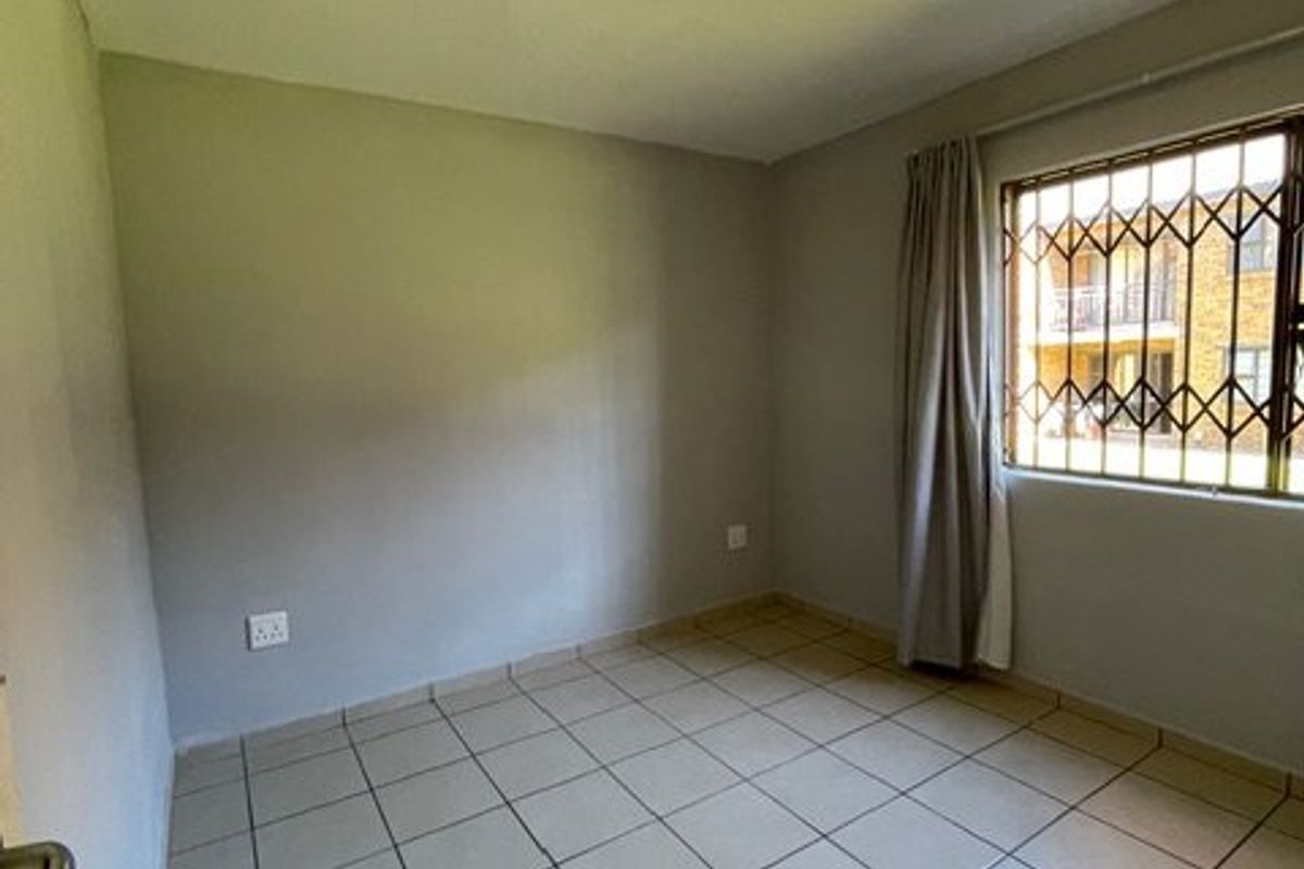 An empty bedroom featuring neutral tiled flooring, a ceiling light fixture, and a window fitted with security bars.