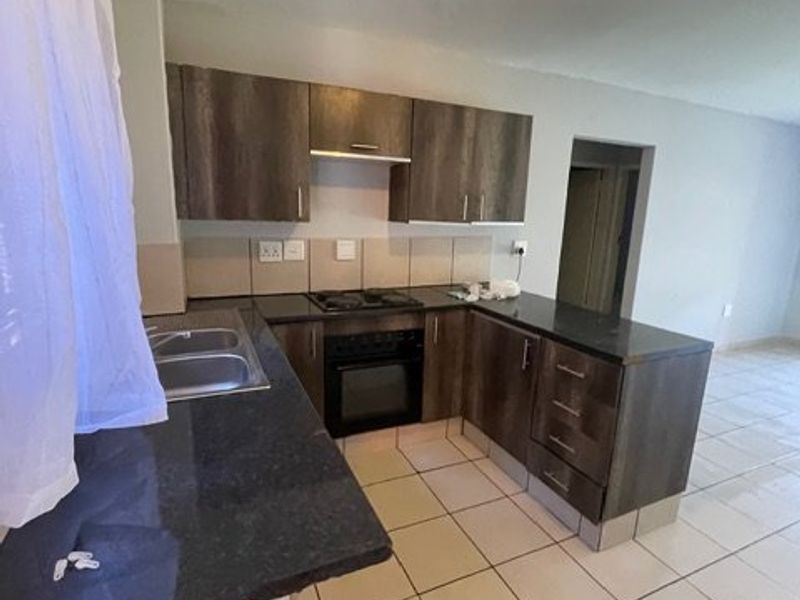 A functional kitchen featuring dark wood cabinetry, granite countertops, a built-in oven and hob, and neutral tiled flooring.