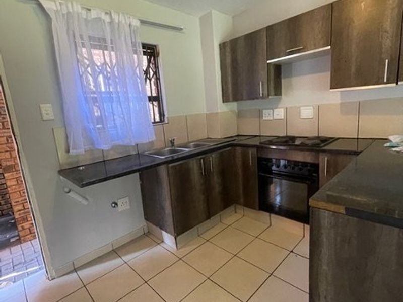 A functional kitchen featuring dark wood-look cabinetry, laminate countertops, built-in oven and hob, and tiled flooring with a neutral backsplash.